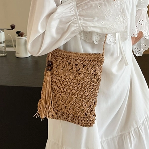 Brown hand-woven straw crossbody bucket bag with floral hollow patterns and tassel detail