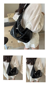 Détail du sac croissant noir brillant avec texture plissée et breloque argentée