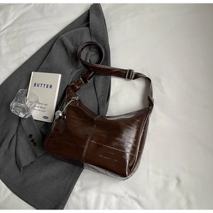 Détail du sac bandoulière marron foncé en simili cuir crocodile avec breloque argentée