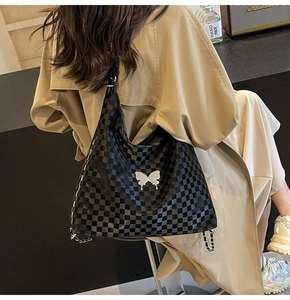 Detail of checkered tote bag featuring a silver butterfly charm and chain shoulder strap