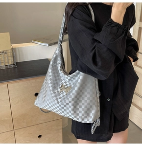 Detail of silver checkerboard tote bag with metal butterfly pendant on model