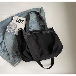 Flat lay of black canvas tote bag with adjustable strap beside a denim jacket