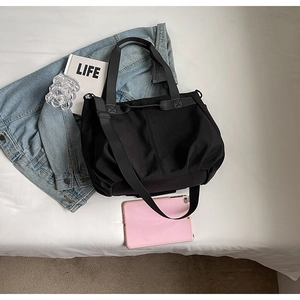 Top-down view of a black large tote bag with laptop and books on a white bed sheet
