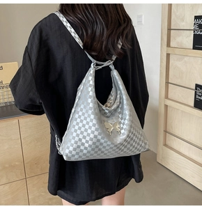 Close-up of silver checkerboard tote bag with butterfly emblem and metallic finish detail