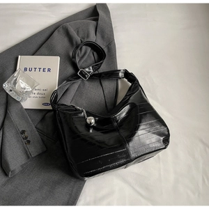 Détail du sac hobo noir brillant montrant la texture gaufrée et le charm en argent