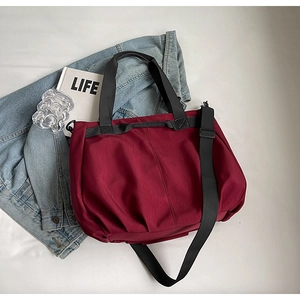Detail view of large burgundy canvas tote bag with black straps and pleated side texture