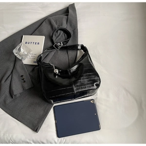 Sac hobo noir plissé avec pendentif argenté posé sur un blazer gris près d'une tablette