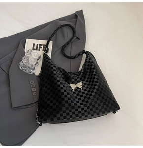 Macro view of black checkerboard tote bag featuring a silver metal butterfly ornament
