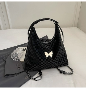 Detail of black checkerboard tote bag with white butterfly charm and metal chain strap