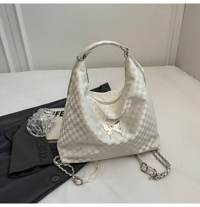 Detail of white checkered tote bag with silver butterfly emblem and chain strap on desk