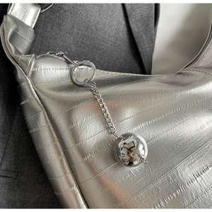 Vue macro du sac à bandoulière argenté montrant le grain texturé et la boule miroir
