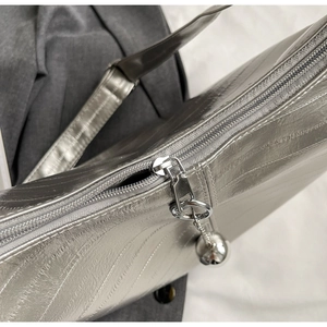 Détail d'un sac argenté texturé montrant la fermeture éclair et le pendentif boule en métal