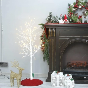 Illuminated white birch tree with warm LED lights and red knitted Christmas tree skirt