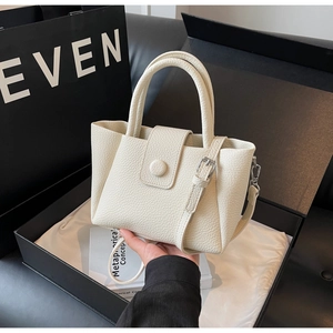 Detailed view of cream white pebble leather handbag with round handle on a gift box