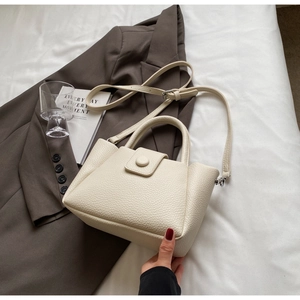 Close-up of cream leather bucket bag with pebble texture and round buckle detail