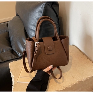 Close-up of brown litchi pattern leather handbag on a stone surface with soft lighting