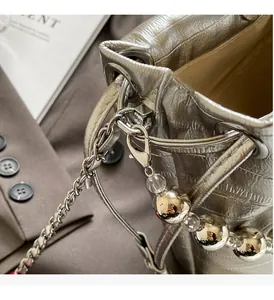 Macro detail of metallic silver bucket bag showing beaded chain and glossy texture