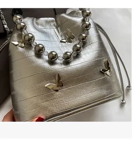 Detail of silver bucket bag featuring metallic texture, butterfly charms and beaded handle
