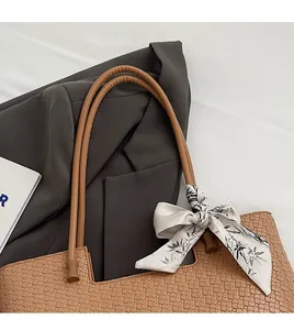 Détail d'un cabas tressé marron avec fines bandoulières et foulard en soie à fleurs