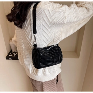 Detail of a black rhinestone cylinder crossbody bag with silver chain strap and zipper