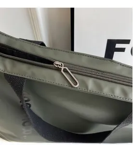 Detail of silver metal zipper puller and black strap on olive nylon tote bag