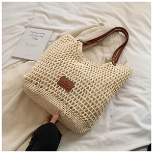 Detail of hollow-out woven tote bag with brown leather handles and logo patch