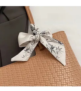 Gros plan d'un foulard en soie à motif bambou noué sur l'anse d'un sac à main tressé