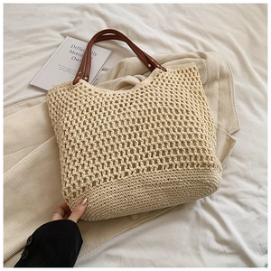 Close-up of beige crochet tote bag with brown leather handles and woven mesh texture