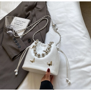Macro view of white croc-embossed bucket bag with silver butterfly and pearl handle