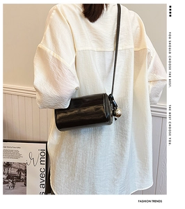 Detail of a glossy black cylindrical crossbody bag with silver sphere charm and leather strap