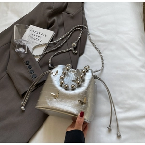 Detail of silver crocodile-pattern bucket bag with beaded handle and butterfly charm