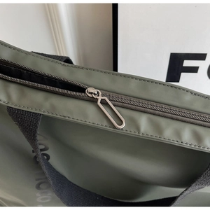 Detail of green nylon tote bag featuring smooth zipper and reinforced canvas strap