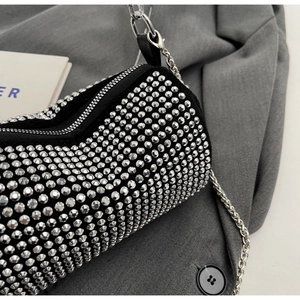 Close-up of sparkling silver rhinestone cylinder bag with metallic chain and zipper detail