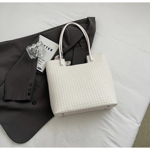 Gros plan sur un cabas blanc tissé sur un blazer gris avec pieds de sac en métal