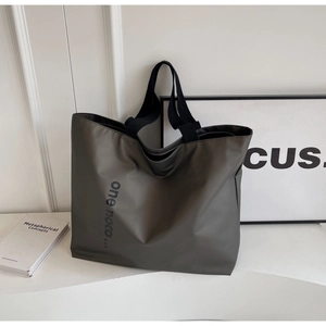 Detailed close-up of dark grey-green nylon tote bag with artistic typography on a minimalist desk