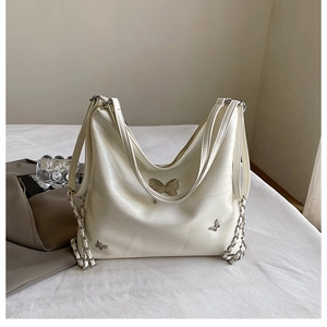 Dettaglio della fibbia a farfalla argento su borsa hobo crema con trama martellata e catena