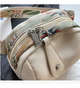 Close-up of cream canvas bag with colorful floral jacquard strap and silver zippers