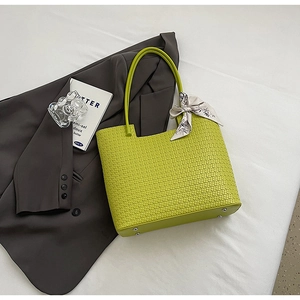 Détail d'un sac cabas tissé vert citron avec foulard en soie sur fond de costume gris