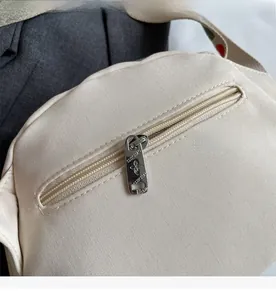 Detailed close-up of smooth metal zipper pocket on the back of beige canvas shell bag
