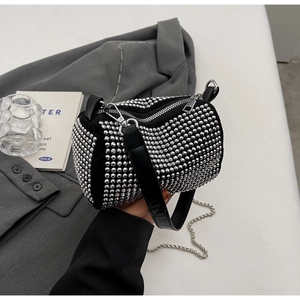 Close-up of black cylinder bag with silver rivets, leather handle and metal chain strap