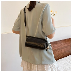 Detail of black cylinder bag in glossy patent leather with silver metallic ball charm