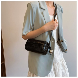 Detail of a black glossy cylinder bag featuring wrinkled leather texture and silver charm