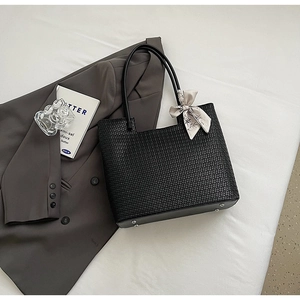 Détail d'un cabas tressé noir avec pieds en métal et accessoire foulard floral élégant