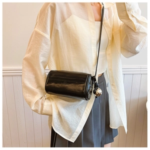 Detail of black glossy cylindrical bag featuring silver metal ball charm and croc texture