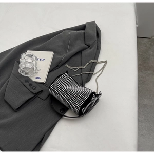 Detail of a mini cylindrical rhinestone crossbody bag on a gray blazer background