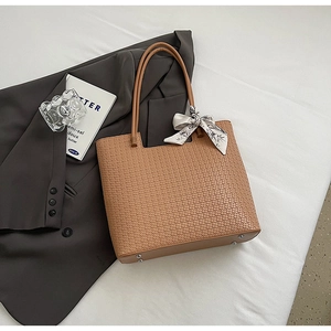 Détail d'un cabas tressé marron montrant les anses en cuir, le foulard et les pieds de protection