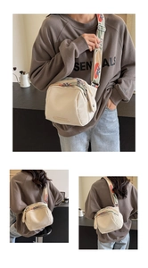 Detail view of cream canvas shell bag featuring a colorful embroidered wide shoulder strap