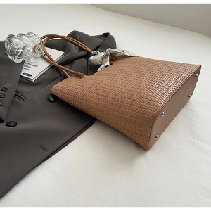 Détail d'un cabas tressé marron avec foulard décoratif en soie et pieds de protection