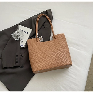 Détail d'un sac cabas marron tissé avec pieds de protection en métal sur blazer gris