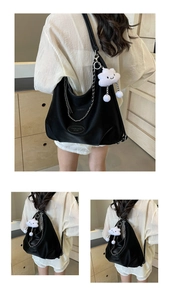 Detail of black dumpling bag in litchi leather with metal chain and plush charm